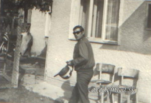 Stará fotografia muža v tmavých okuliaroch kráčajúceho po dvore s motorkárskou prilbou v ruke